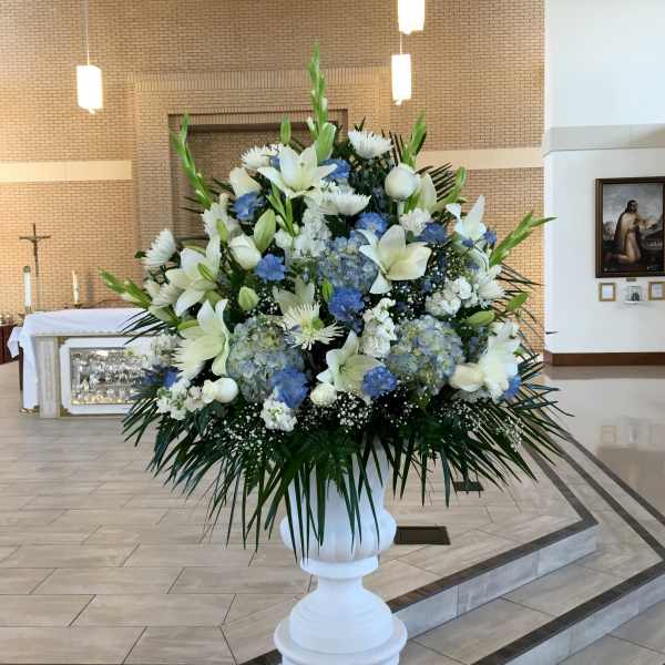 Large white and blue floral arrangement in a white pedestal vase