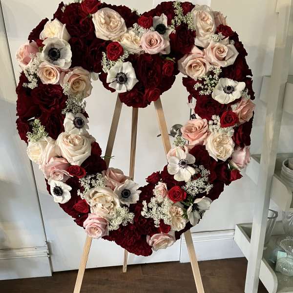 Heart-shaped floral wreath of red, blush, and white roses on an easel