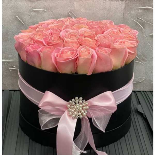 Round black hat box filled with pink roses and tied with a pink bow and pearl brooch.