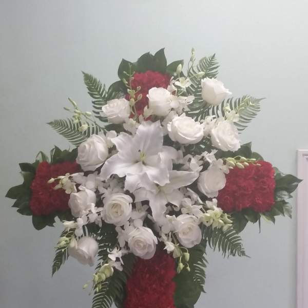 Cross-shaped floral spray with white lilies and roses and red flowers