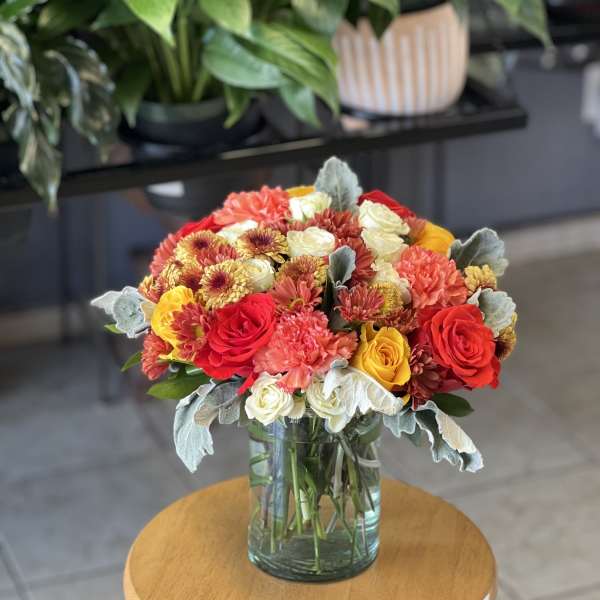 Mixed bouquet of red, yellow, white, and peach flowers in a glass vase