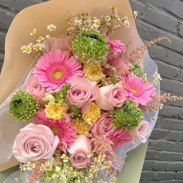 Bouquet of pink roses, gerbera daisies, and green blooms wrapped in paper