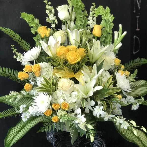 White and yellow floral arrangement in a black pedestal vase
