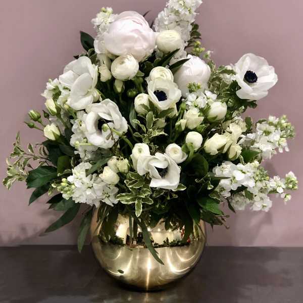 White floral arrangement in a gold vase with anemones and ranunculus