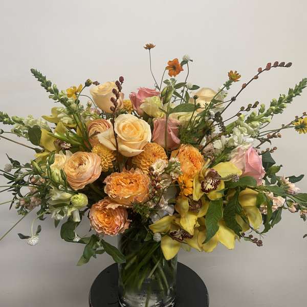 Large mixed bouquet of roses, orchids, and yellow blooms in a glass vase