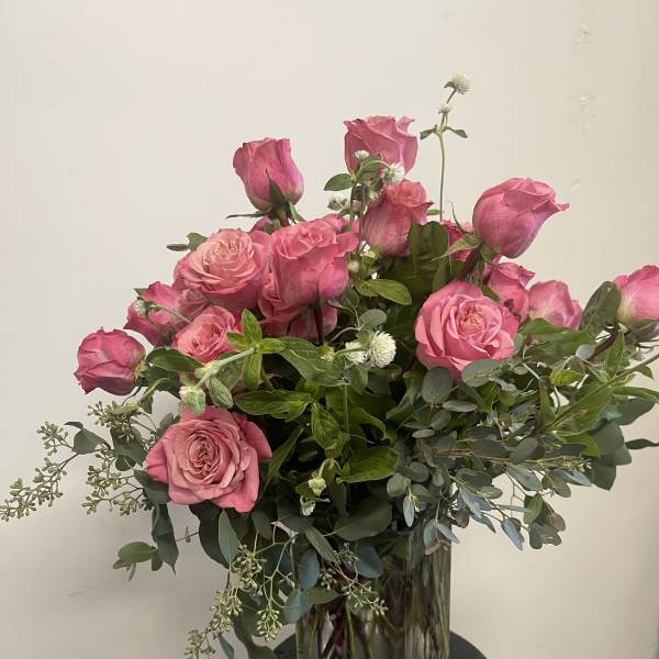 Pink roses arranged in a clear glass vase with greenery