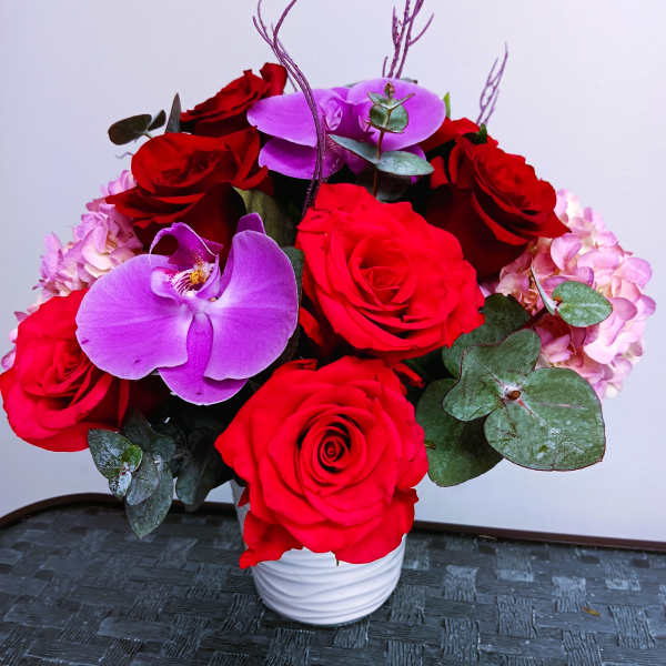 Red roses and purple orchids in a white vase