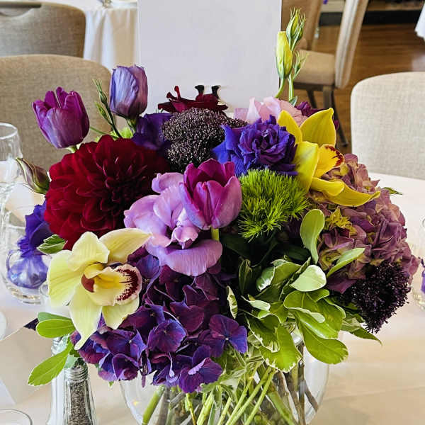 Mixed bouquet of purple, pink, yellow, and red flowers in a glass vase
