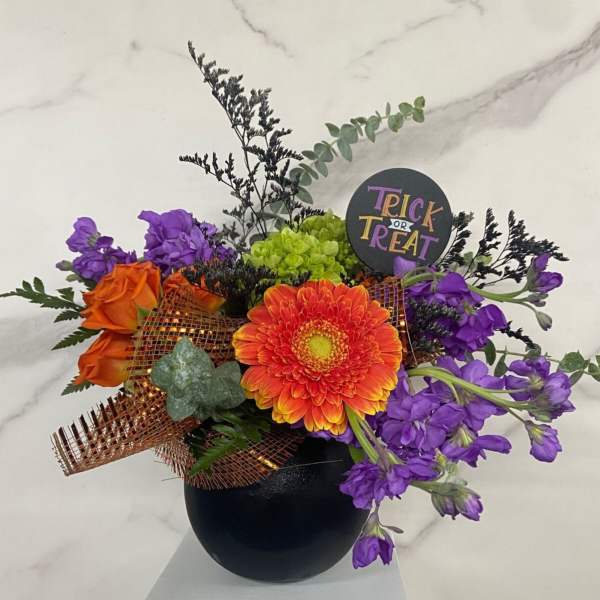 Orange and purple floral arrangement in a black vase with a Trick or Treat sign