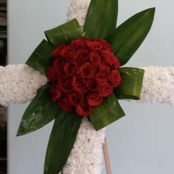 Red rose arrangement on a white floral cross with green leaves