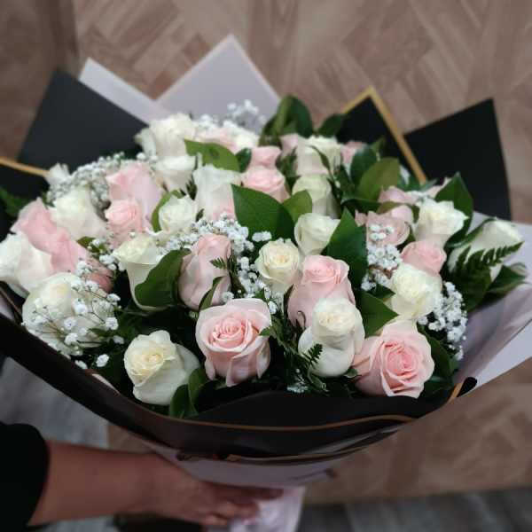 Bouquet of pale pink and white roses wrapped in black paper