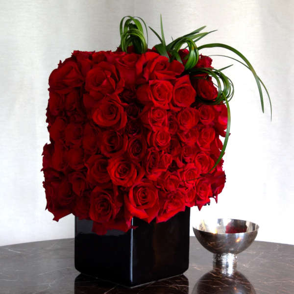 Red rose arrangement in a black vase with curled green leaves
