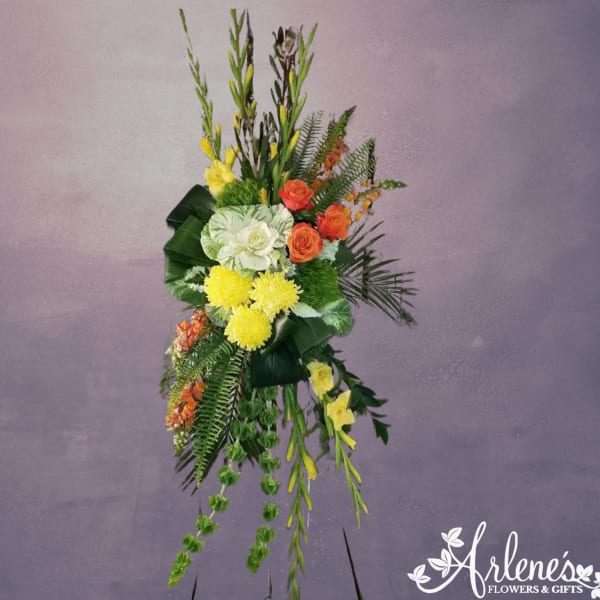 Tall standing spray with yellow mums, orange roses, white cabbage blooms and Bells of Ireland on an easel.
