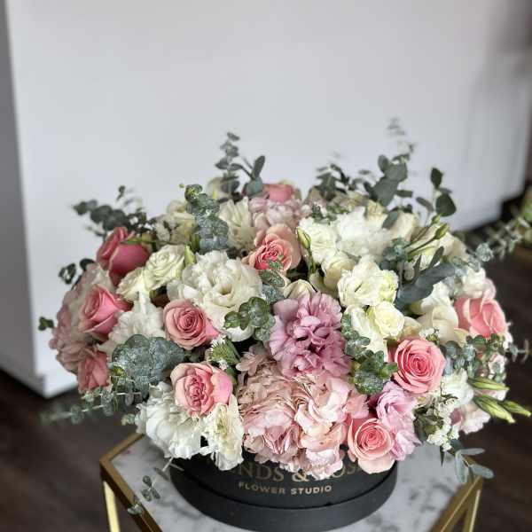 Round bouquet of pink and white roses with pale hydrangeas in a black box