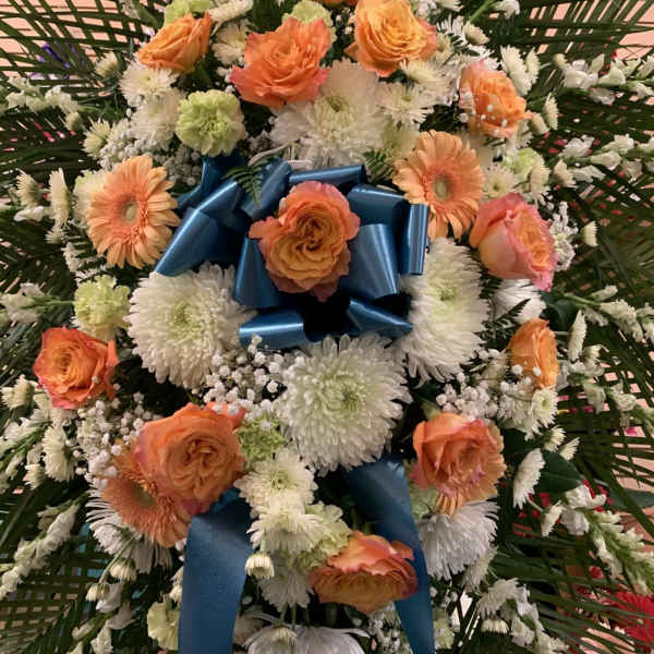 Large floral standing spray with orange roses and white daisies, finished with a blue ribbon