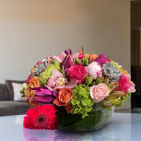 Round bouquet of pink, orange, purple, and green flowers in a glass bowl.