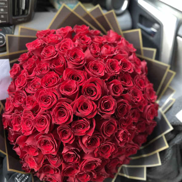Large round bouquet of tightly packed red roses wrapped in layered black and gold paper.