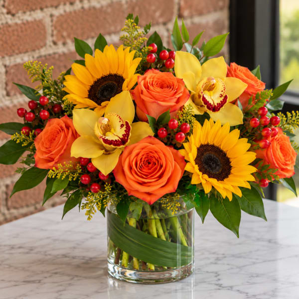 Bouquet of orange roses, sunflowers, and yellow orchids in a glass vase
