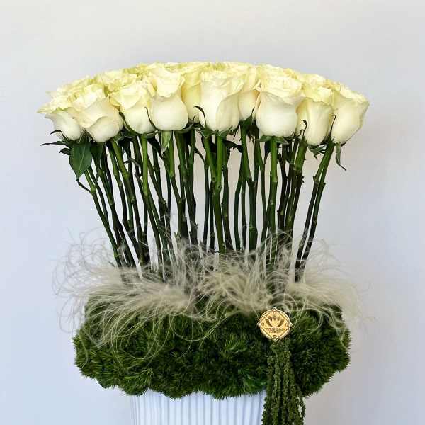 Tall arrangement of white roses in a white vase with green moss
