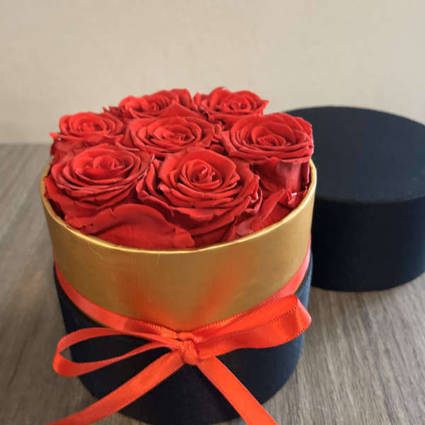 Red roses arranged in a round black box with a gold band and red ribbon