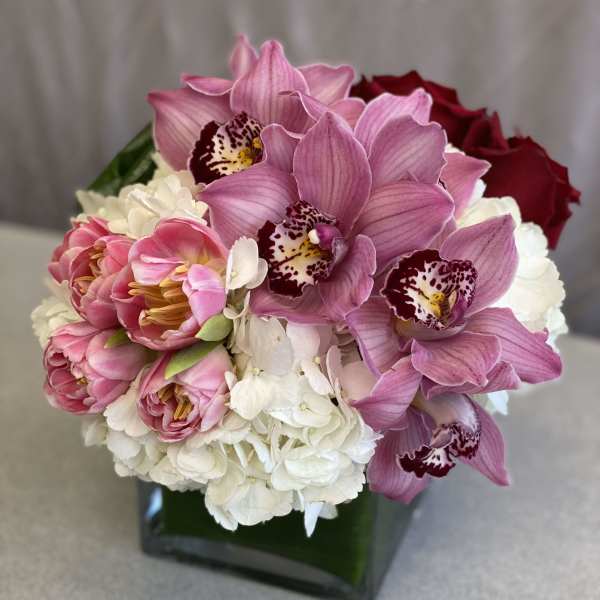 Pink orchids and roses arranged in a square glass vase