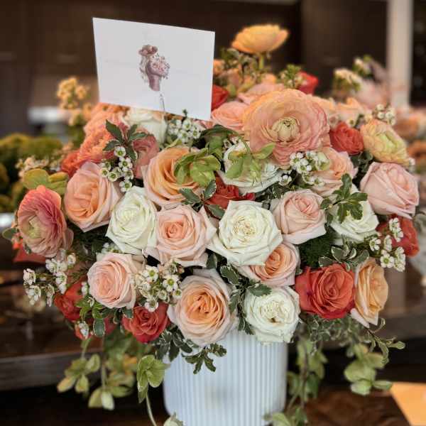 Large bouquet of peach, pink, and white roses in a white vase