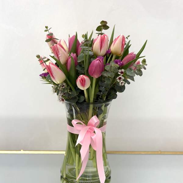 Pink tulips in a clear glass vase with a pink ribbon