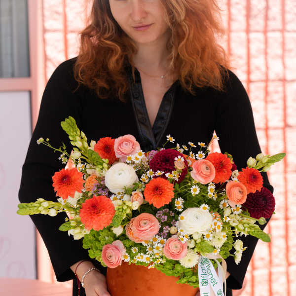 Woman holding a large mixed flower arrangement in an orange box