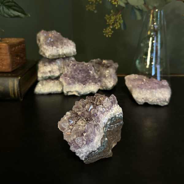 Purple crystal clusters on a dark surface with a glass vase of stems in the background