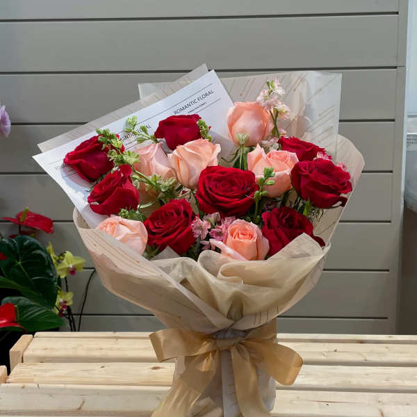 Bouquet of red and blush roses wrapped in cream paper with a gold ribbon