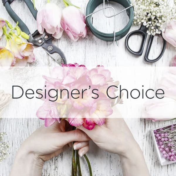 Hands hold a pink flower bouquet with floral tools and supplies around it.