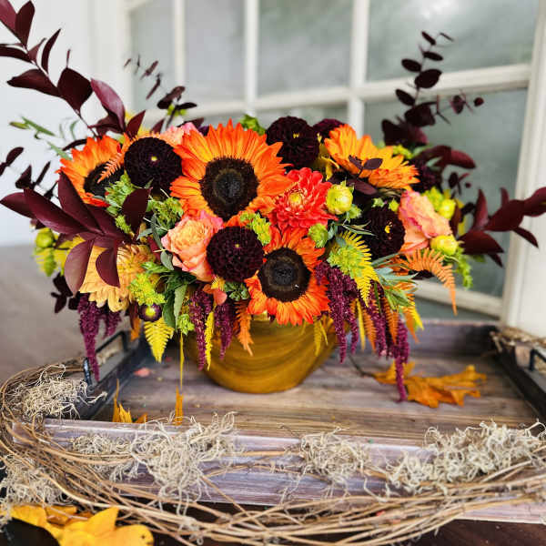 Autumn bouquet with sunflowers, orange blooms, and burgundy foliage in a gold vase