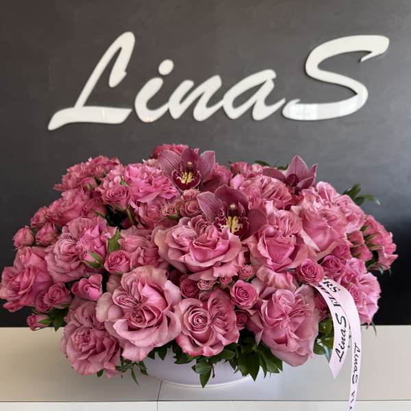Large pink rose arrangement with orchid blooms in a white container
