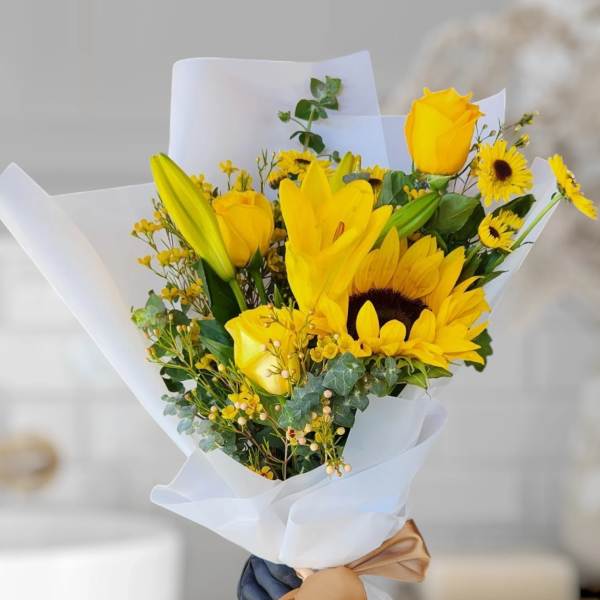 Yellow bouquet with roses, lilies, and sunflowers wrapped in white paper