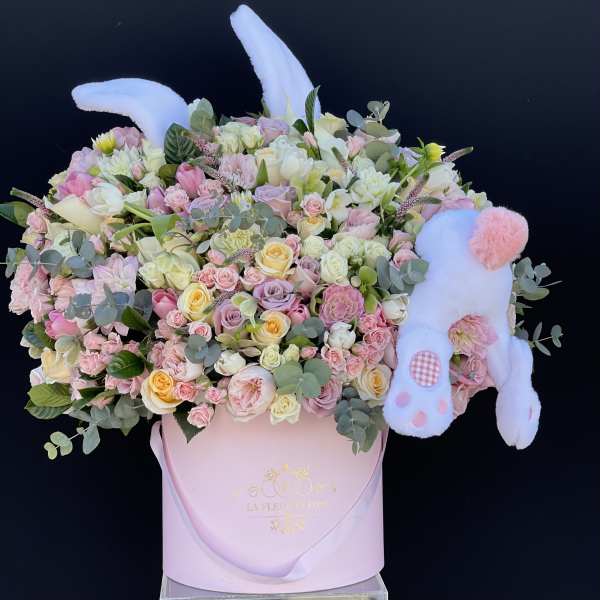 Pastel flower arrangement in a pink box with a plush bunny
