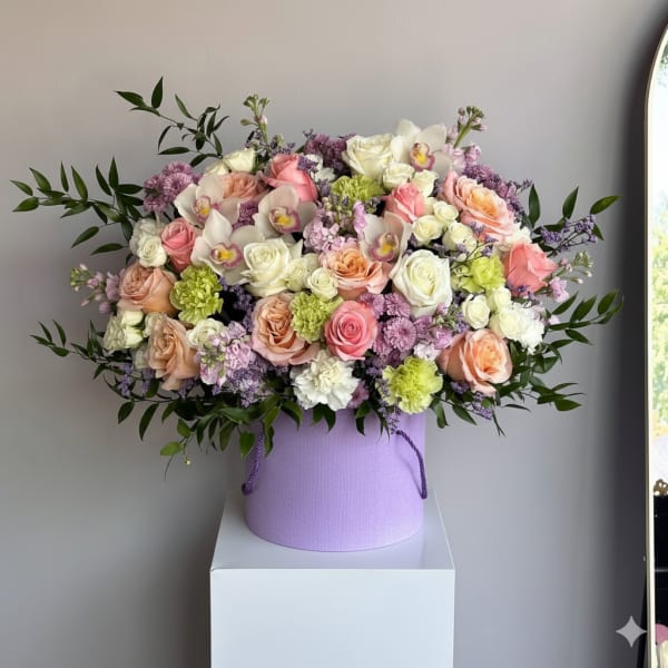 Large pastel arrangement of roses, orchids and mixed blooms in a lavender hatbox-style container