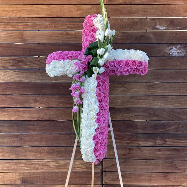 Cross-shaped floral arrangement of pink and white roses on an easel