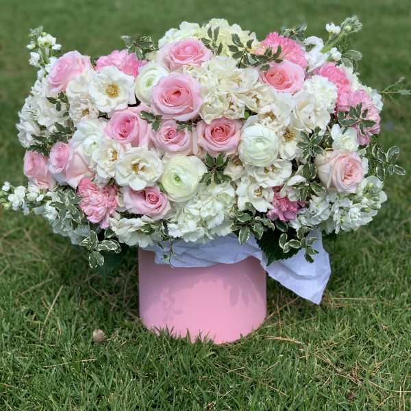 Pink and white floral arrangement in a pink box on grass