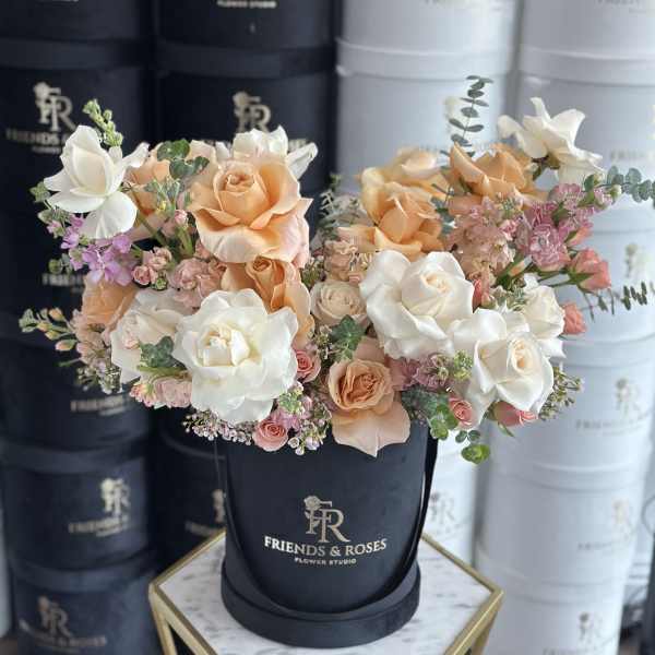 Peach and white roses with small pink flowers in a black hatbox.