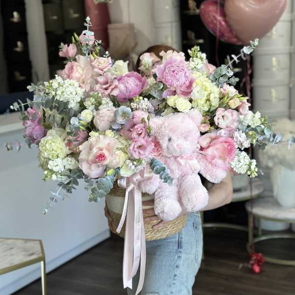 Large pink and white flower arrangement with a teddy bear in a woven basket