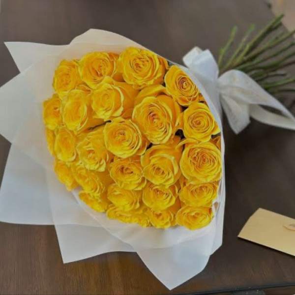 Bouquet of bright yellow roses wrapped in white paper with a ribbon on a table.