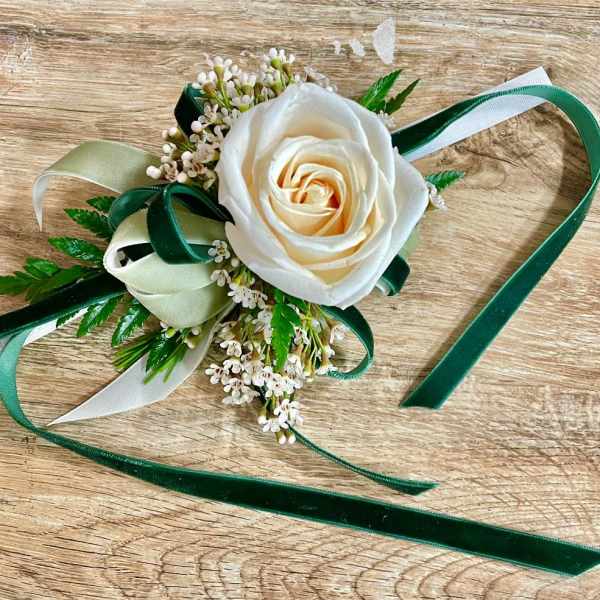 White rose corsage with green and ivory ribbons on a wooden surface