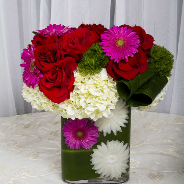 Red roses and pink daisies in a green vase with white hydrangeas