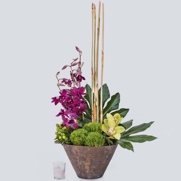 Purple orchids and yellow orchids in a tall brown vase with bamboo sticks