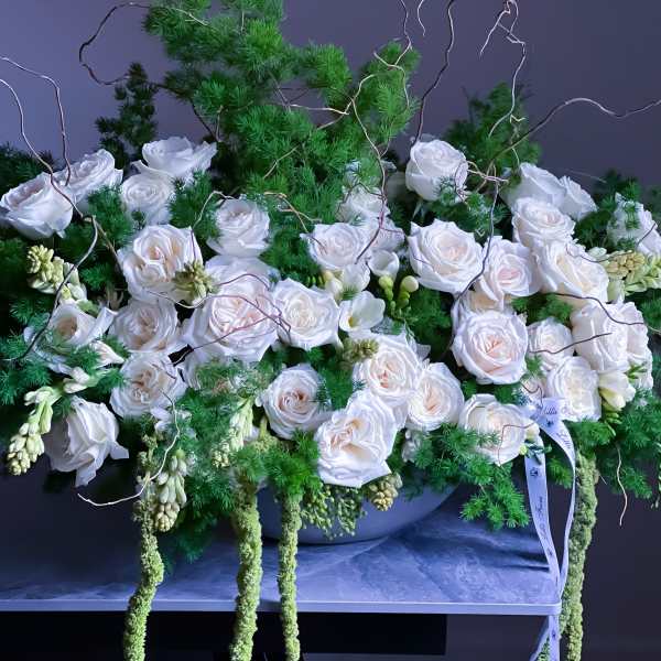 White roses arranged with green foliage in a low container