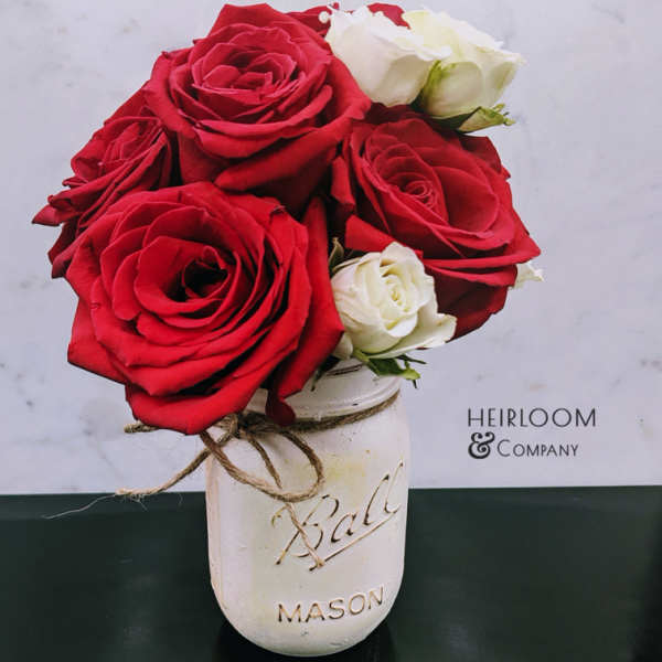 Red and white roses in a white mason jar vase