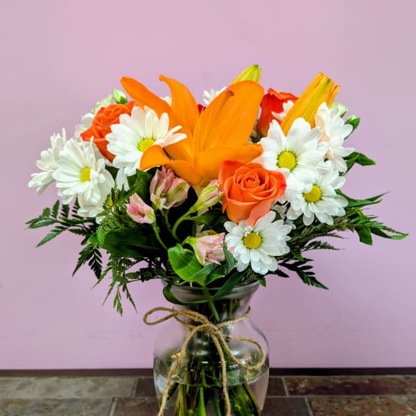 Orange lilies and daisies in a glass vase with twine