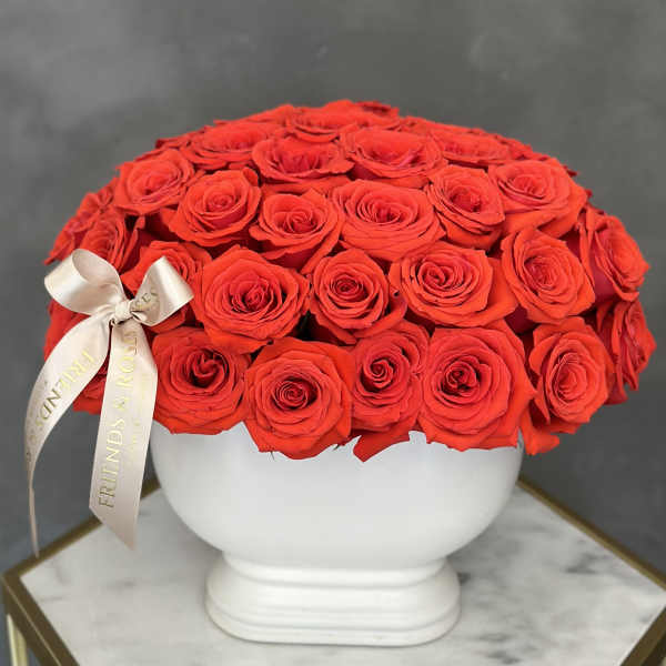 Round arrangement of red roses in a white vase with a satin ribbon