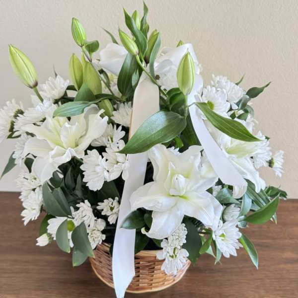 White lilies and daisies arranged in a wicker basket with a white ribbon