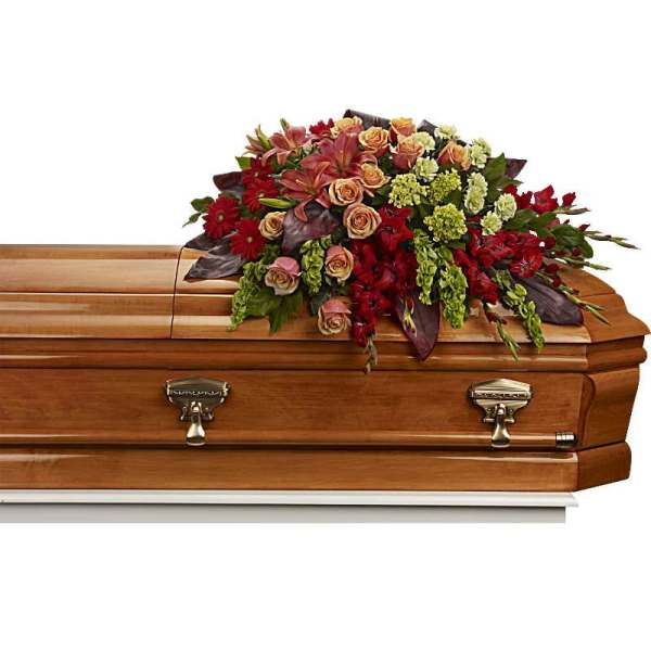 Casket spray with red and peach flowers on a wooden casket